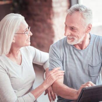 two older people sitting while looking at a laptop